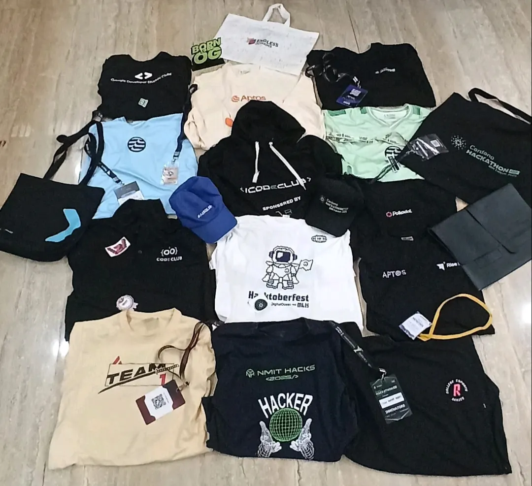 A pile of hackathon t-shirts, bags and badges